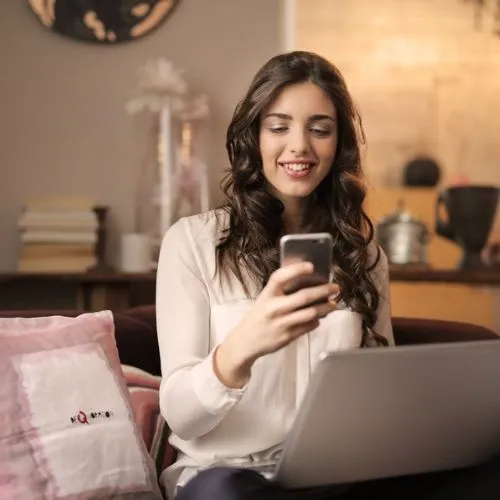alt="Image of girl sitting at her desk with a phone in her hand"